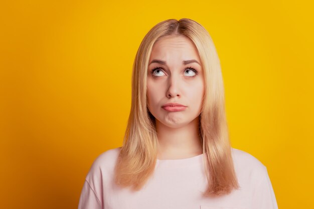 Portret van bedachtzame twijfelachtige dame opzoeken lege ruimte op gele achtergrond