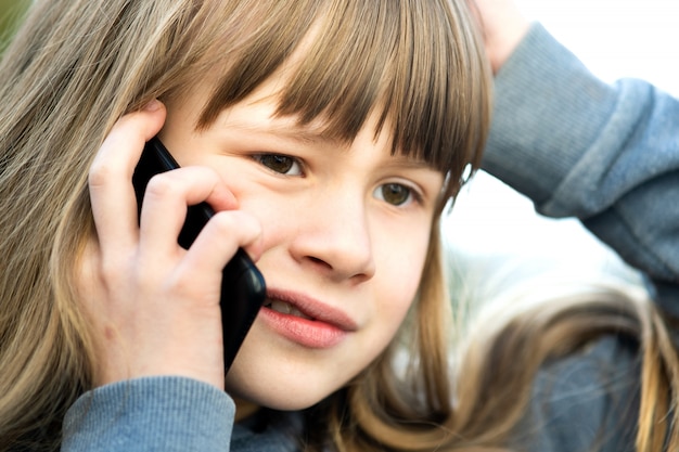 Portret van beklemtoond kindmeisje met lang haar dat op celtelefoon spreekt. Kleine vrouwelijke jongen communiceren via smartphone. Kinderen communicatieconcept.