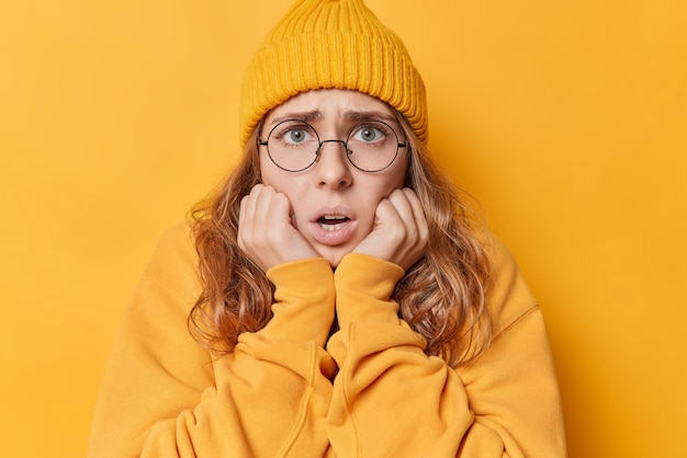 Portret van beschaamde geschokte jonge vrouw staart nerveus houdt handen onder de kin en mondt uit in paniek gekleed in vrijetijdskleding geïsoleerd over levendige gele achtergrond. mensen en reacties