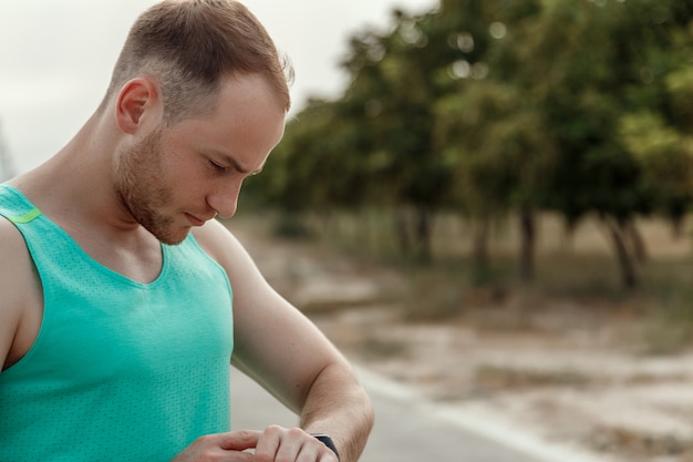 Portret van blanke man in azuurblauwe t-shirt kijken naar fitness tracker lezingen