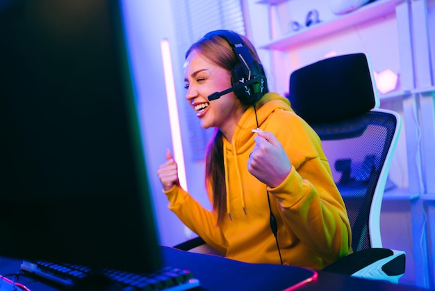 Portret van blanke vrouwelijke gamer in gele hoodie die overwinning viert voor speeltafel Gamer die een esports-game wint met overwinningsemotie De speler verheugt zich over de overwinning in de competitie