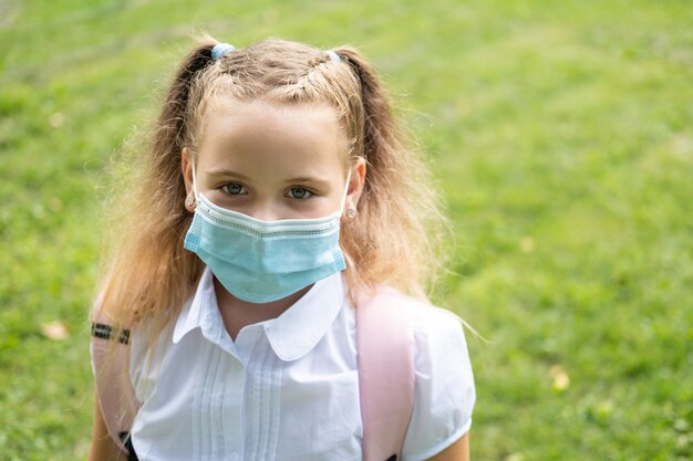 Portret van blond krullend schoolmeisje met beschermend masker in schooluniform met roze rugzak terug naar school.