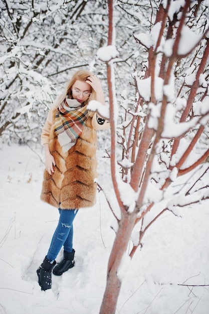 Portret van blond meisje in glazen, rode bontjas en sjaal op winterdag.