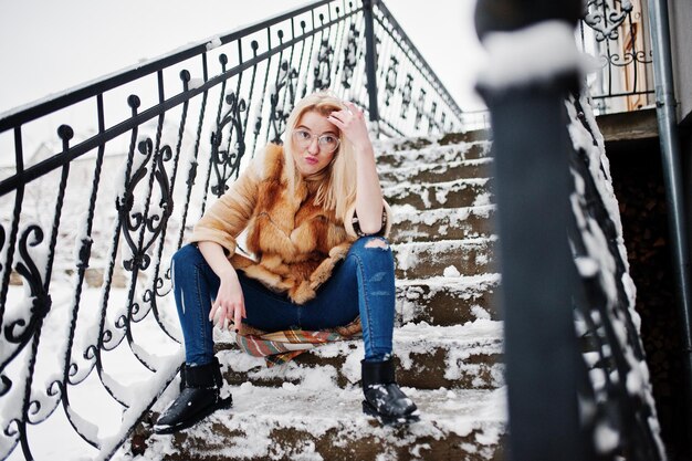 Portret van blond meisje in glazen, rode bontjas en sjaal op winterdag.