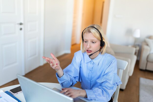 Portret van blonde vrouw die videogesprek voert met behulp van laptop Zakenvrouw met hoofdtelefoon die praat tijdens online ontmoeting met collega Albino-vrouw die vanuit huis werkt via een videoconferentie op computer