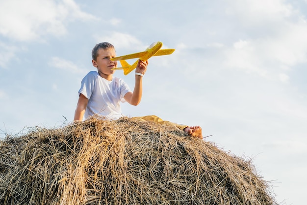 Portret van blote voeten jongen in hoed op hooiberg in veld Spelen met speelgoedvliegtuig Lichte zonnige dag Outdoor