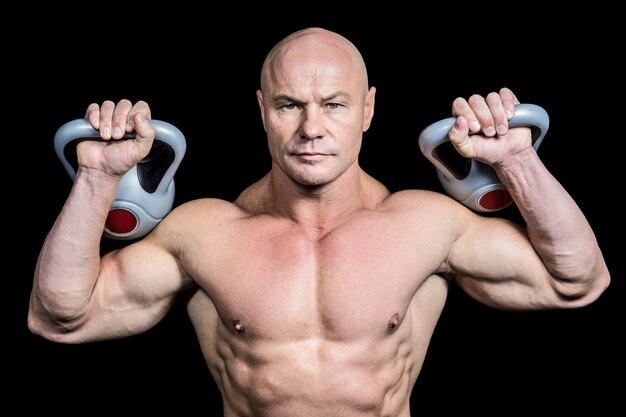 Portret van bodybuilder opheffende kettlebells tegen zwarte achtergrond