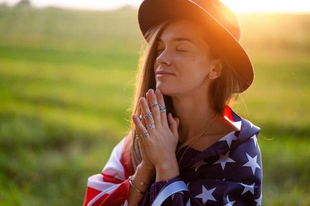 Foto portret van boho chique vrouw in hoed met amerikaanse vlag die zilveren ringen met turkooise steen dragen bij zonsondergang. sieraden indie meisje met hippie stijl en boho mode. reis naar amerika