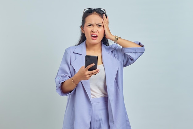 Portret van boze jonge aziatische vrouw die smartphone vasthoudt en naar camera kijkt die op witte achtergrond wordt geïsoleerd