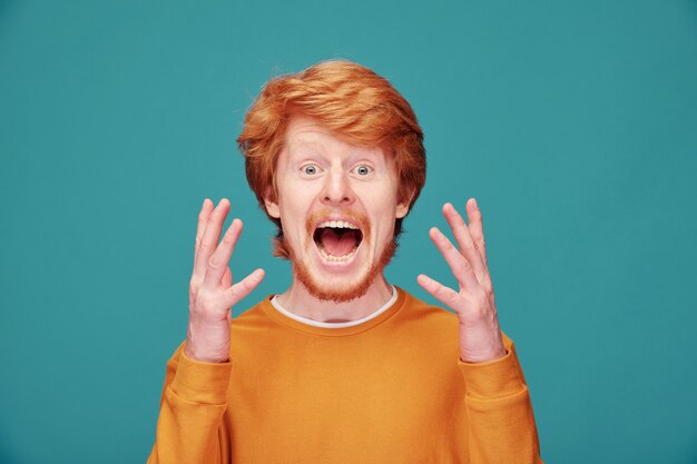 Foto portret van boze roodharige man met baard fronsend gezicht in agressie tegen blauwe muur