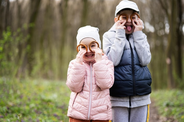 Portret van broer met zus die bagels vasthoudt in de buurt van ogen met grappige gezichten in het lentebos