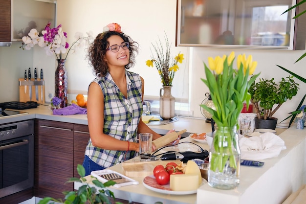 Portret van brunette aantrekkelijke vrouw met krullend haar in een huiskeuken met veel bloemen.