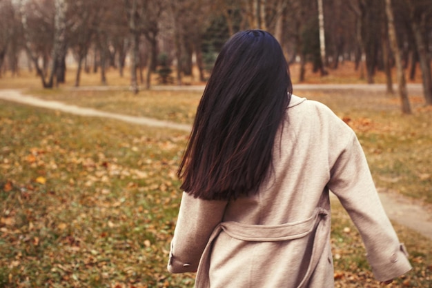 Portret van brunette haar vrouw in beige jas wandelen in het stadspark