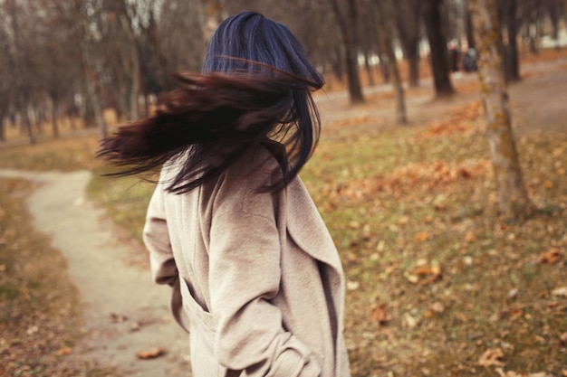 Portret van brunette haar vrouw in beige jas wandelen in het stadspark