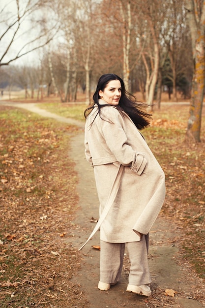 Portret van brunette haar vrouw in beige jas wandelen in het stadspark