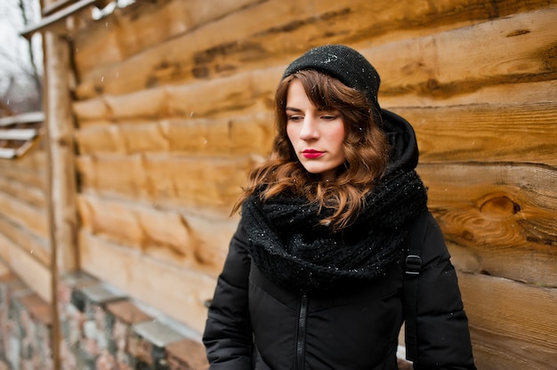 Portret van brunette krullend meisje in zwarte jas, hoed en sjaal op winterdag.