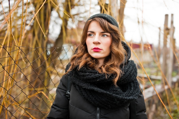 Portret van brunette krullend meisje in zwarte jas, muts en sjaal op winterdag.