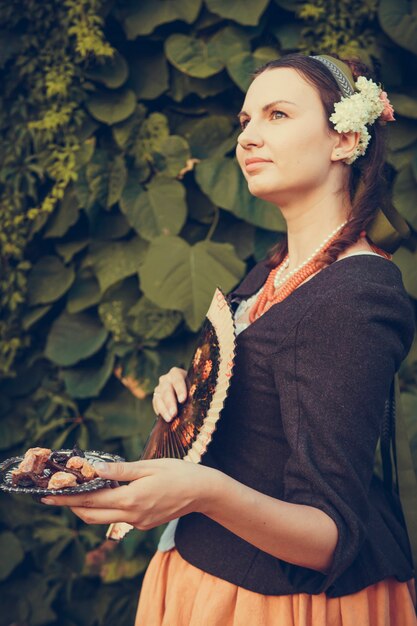 Foto portret van brunette vrouw gekleed in historische barokke kleding met ouderwets kapsel, buitenshuis. middeleeuwse jurk uit de middenklasse