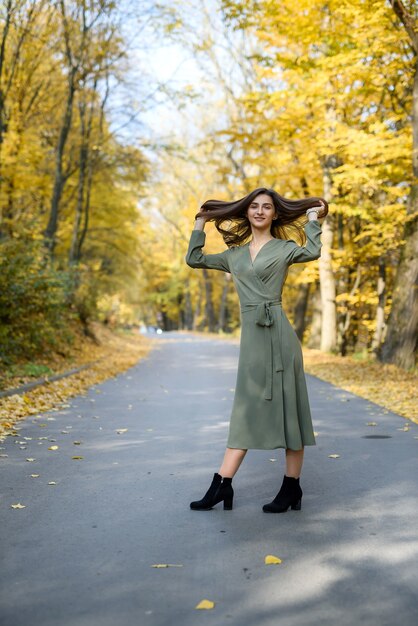 Portret van brunette vrouw in groene jurk poseren in herfst park