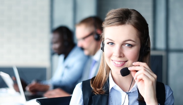 Portret van callcentermedewerker vergezeld door haar team. Glimlachende klantenondersteuningsoperator op het werk.