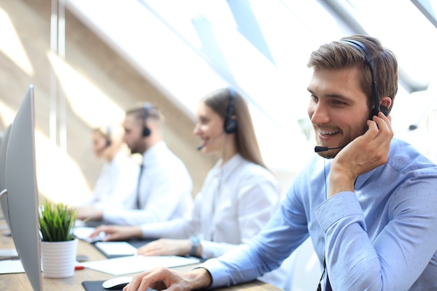 Portret van callcentermedewerker vergezeld door zijn team. Glimlachende klantenondersteuningsoperator op het werk.