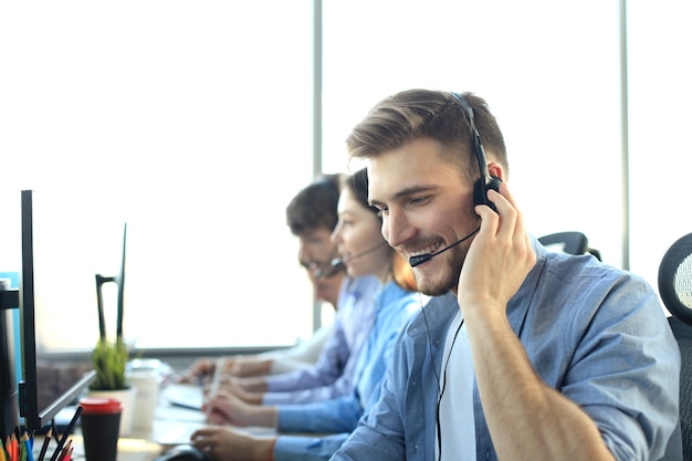 Portret van callcentermedewerker vergezeld door zijn team. Glimlachende klantenondersteuningsoperator op het werk.