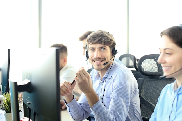 Portret van callcentermedewerker vergezeld door zijn team. Glimlachende klantenondersteuningsoperator op het werk.