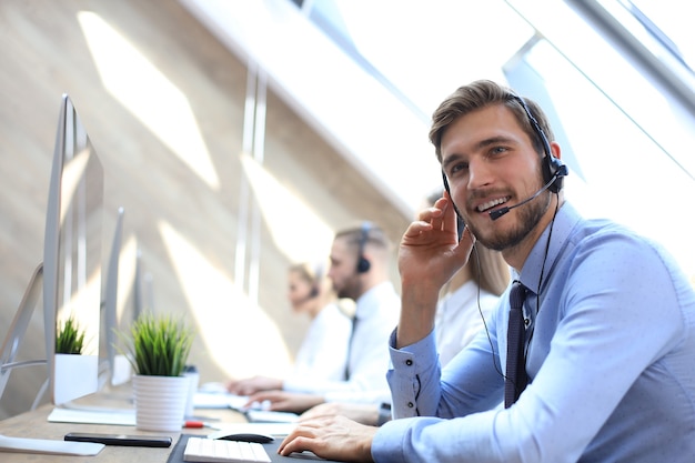 Portret van callcentermedewerker vergezeld door zijn team. Glimlachende klantenondersteuningsoperator op het werk.