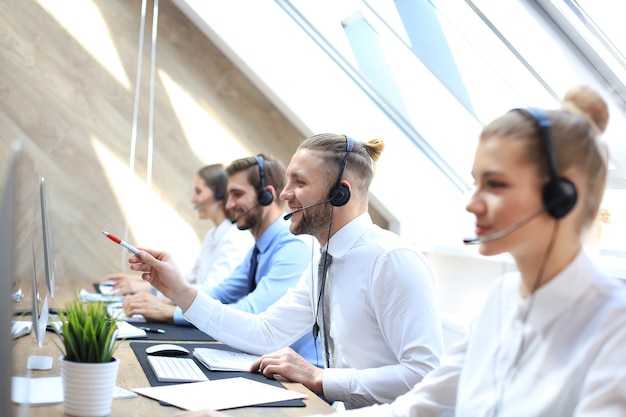 Portret van callcentermedewerker vergezeld door zijn team. Glimlachende klantenondersteuningsoperator op het werk.