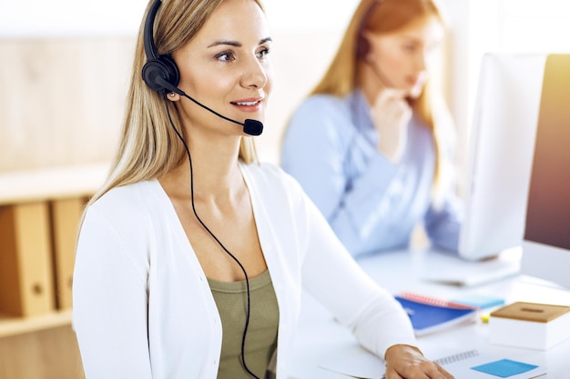 Portret van callcenteroperator aan het werk in zonnig kantoor. Groep mensen in een headset klaar om klanten te helpen. Bedrijfsconcept.