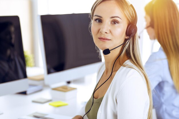 Portret van callcenteroperator aan het werk in zonnig kantoor. Groep mensen in een headset klaar om klanten te helpen. Bedrijfsconcept.