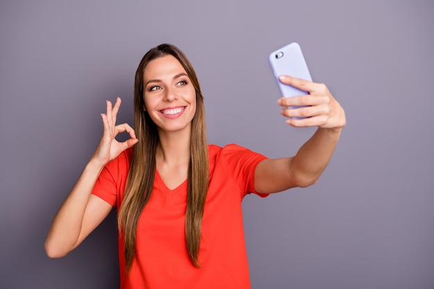 Portret van charmante brunette dame in rood t-shirt poseren tegen de paarse muur met telefoon