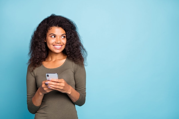 Portret van charmante donkere huid meisje blogger met vrolijke positieve emoties houdt haar mobiele telefoon gebruiken blik dragen casual stijl outfit geïsoleerd over blauwe kleur muur