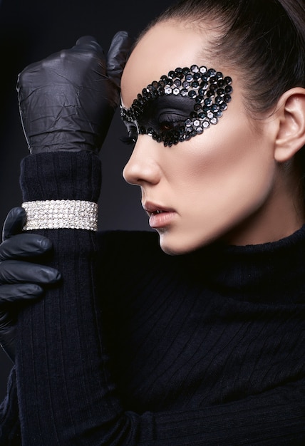 Portret van charmante elegante brunette vrouw in coltrui trui en pailletten masker poseren op zwart in de studio