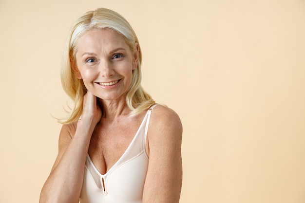 Portret van charmante rijpe vrouw met blond haar in wit ondergoed glimlachend naar camera poseren