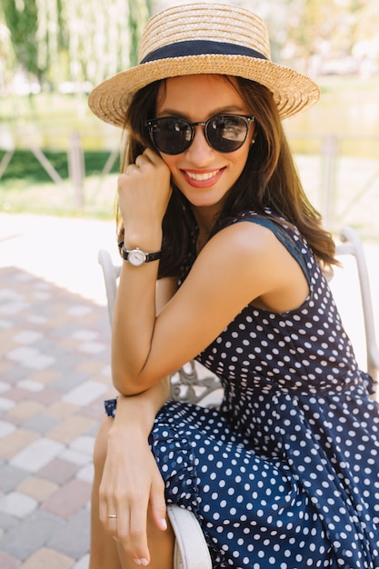 Portret van charmante stijl vrouw in het zomerpark zomer hoed en zwarte zonnebril en schattige jurk dragen.
