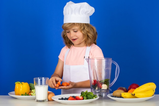 Portret van chef-kok kind in kok hoed houden wortel thuis koken jongen jongen bereiden van voedsel van groente
