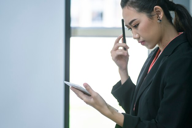 Portret van comfident jonge ondernemersonderneemster die met tablet of mobiel apparaat in werkstation werken.