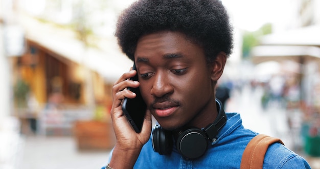 Portret van de aantrekkelijke jonge man die buiten op de smartphone praat terwijl hij de mobiele telefoon gebruikt voor...