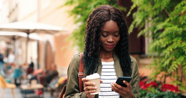 Portret van de aantrekkelijke jonge multiraciale vrouw die smartphone praat en buiten koffie drinkt...