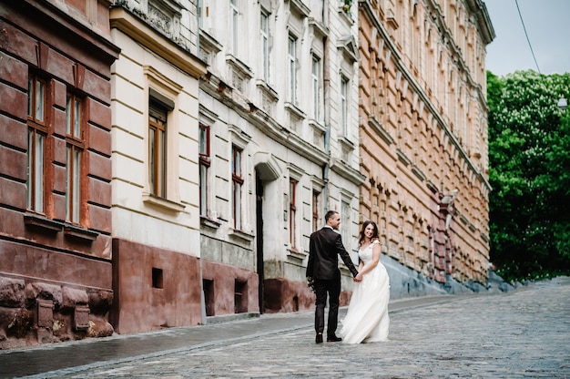 Portret van de bruidegom en de bruid die teruggaan in de buurt van oud gebouw, oud huis buiten, buiten. Jonggehuwden lopen door de straten van de stad Lviv.