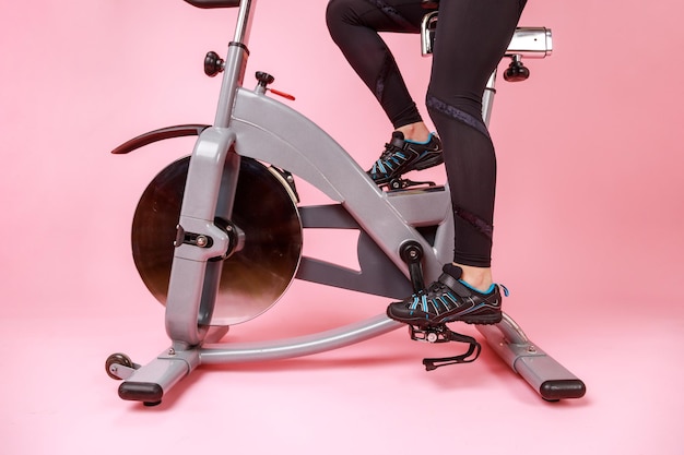 Portret van de fietssimulator en damesbenen in zwarte sneakers en leggins cardiotraining