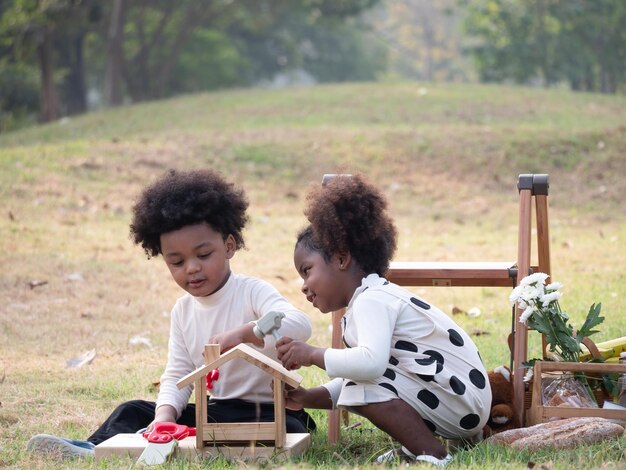 Portret van de gelukkige Afro-Amerikaanse jongens en meisjes die picknicktafel in de tuin zetten in de mooie ochtend Adventure kleuterschool dagtocht naar de wilde natuurxA