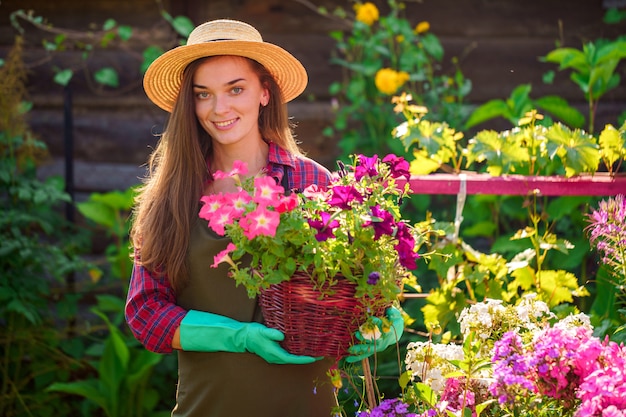 Portret van de gelukkige blije vrouw van de bloemisttuinman in hoed met bloempot van petunia in openlucht. Tuinieren en sierteelt. Groeiende bloem in huistuin