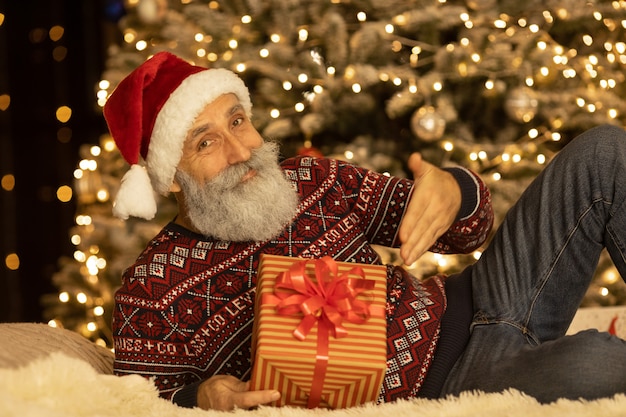 Portret van de gelukkige kerstman op zijn kamer thuis in de buurt van de kerstboom.