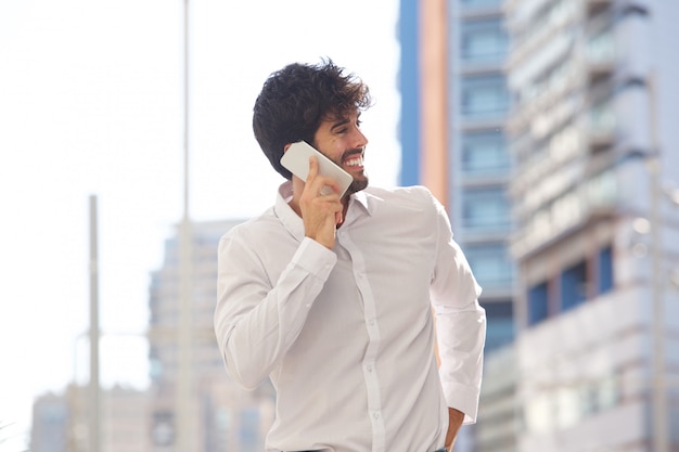 Portret van de gelukkige mens die buiten op slimme telefoon glimlachen spreken en