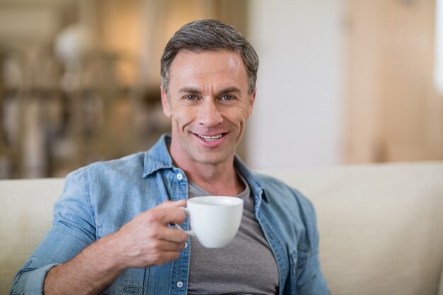 Portret van de glimlachende mens die koffie in woonkamer heeft