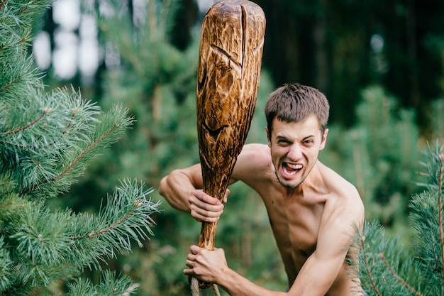 Portret van de grappige man met houten stok en wilde gelaatsuitdrukking jacht in het bos