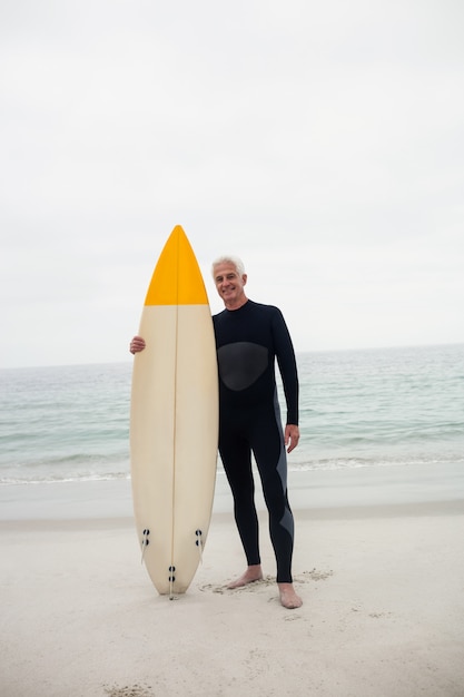 Portret van de hogere mens die in wetsuit een surfplank houdt