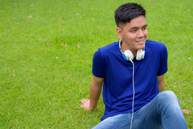 Portret van de jonge knappe Aziatische man ontspannen in het park in Bangkok, Thailand